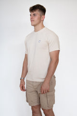 A side on view of a male model wearing a cream cosycore by beCosy short sleeve tshirt with an embroidered cat logo