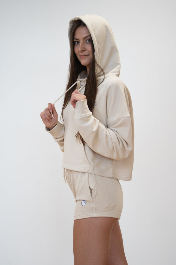 side view of female model wearing cosycore cream cropped hoodie showing off the oversized hood and matching terry shorts