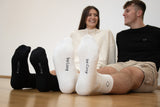 Models wearing the Cosycore crew socks by beCosy showing off the embroidered logo and text on the sole. one pair of socks is black and the other is white
