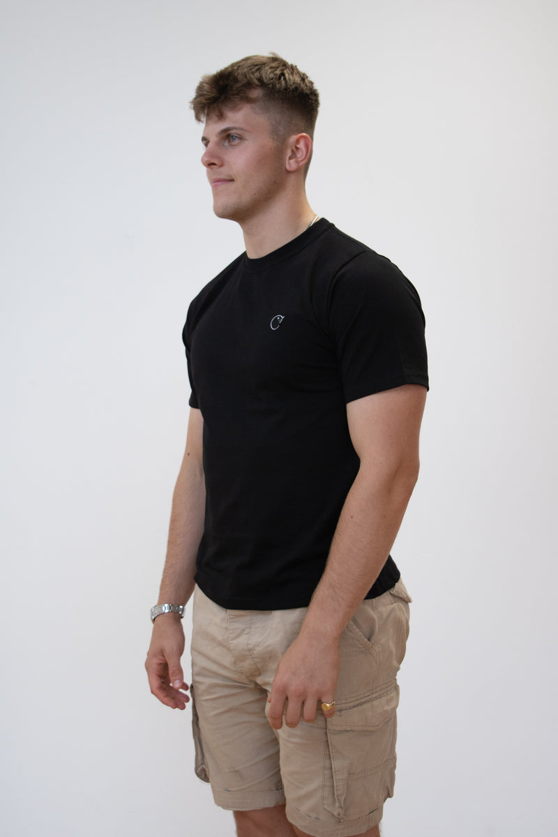A side on view of a male model wearing a plain black cosycore by beCosy short sleeve tshirt with an embroidered cat logo