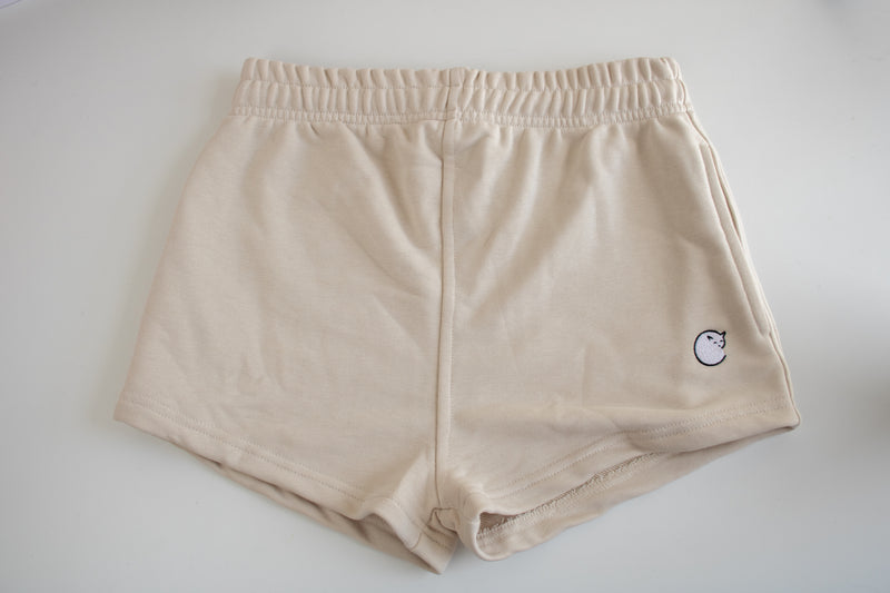top down view of the cosycore terry shorts which are cream and feature an embroidered logo, elasticated waist band, and pockets